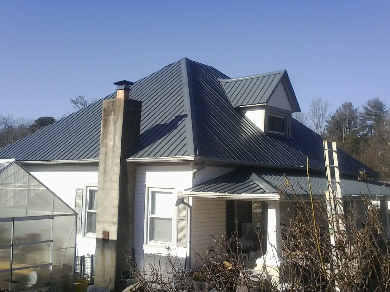 Dark blue standing seam metal roof on a white farmhouse with dormer — Slate & Tile Roof Repair by Roofing Brothers in Pinson