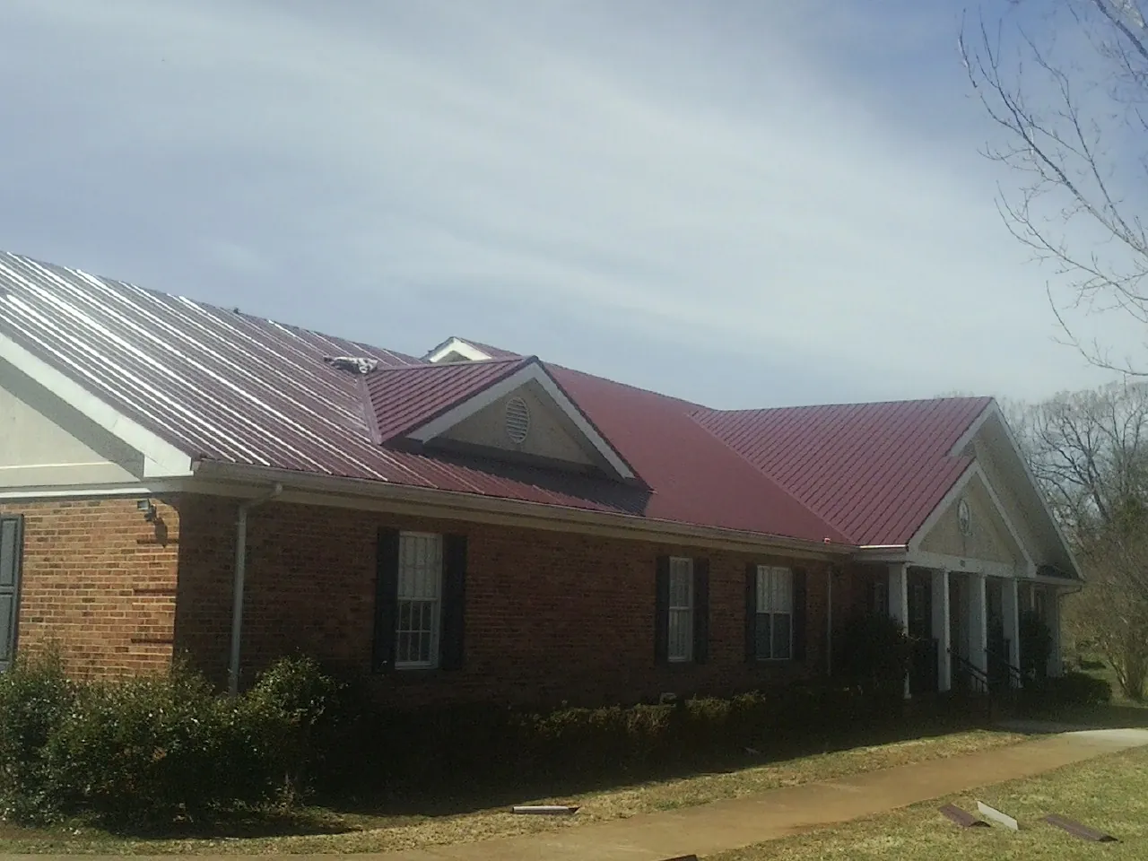 Red metal roof with gabled entries on a long brick building, from a Hail Damage Roof Repair job in Pinson