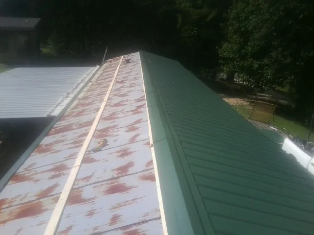 Old rusted panels beside newly installed green metal roofing — Wind Damage Roof Repair by Roofing Brothers in Pinson