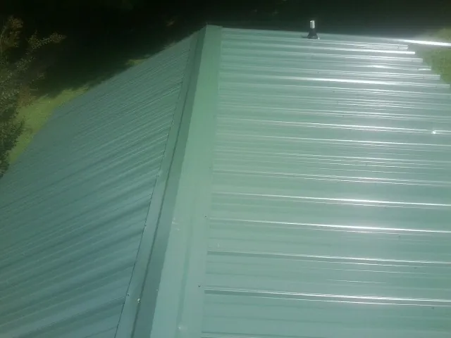 New green metal panels meeting at the ridge of a roof — Flat Roof Repair work by our crew in Pinson