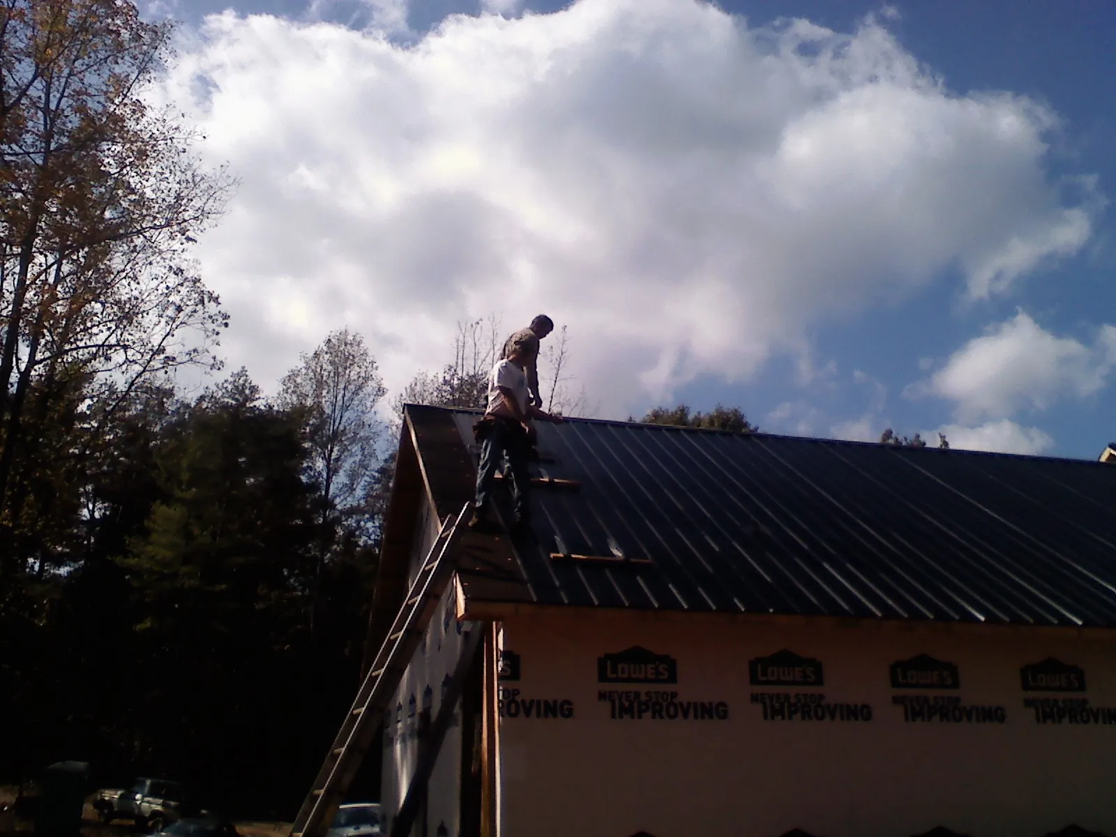 Roofer fastening dark metal panels high against a cloudy sky, from a Roof Inspection job in Pinson