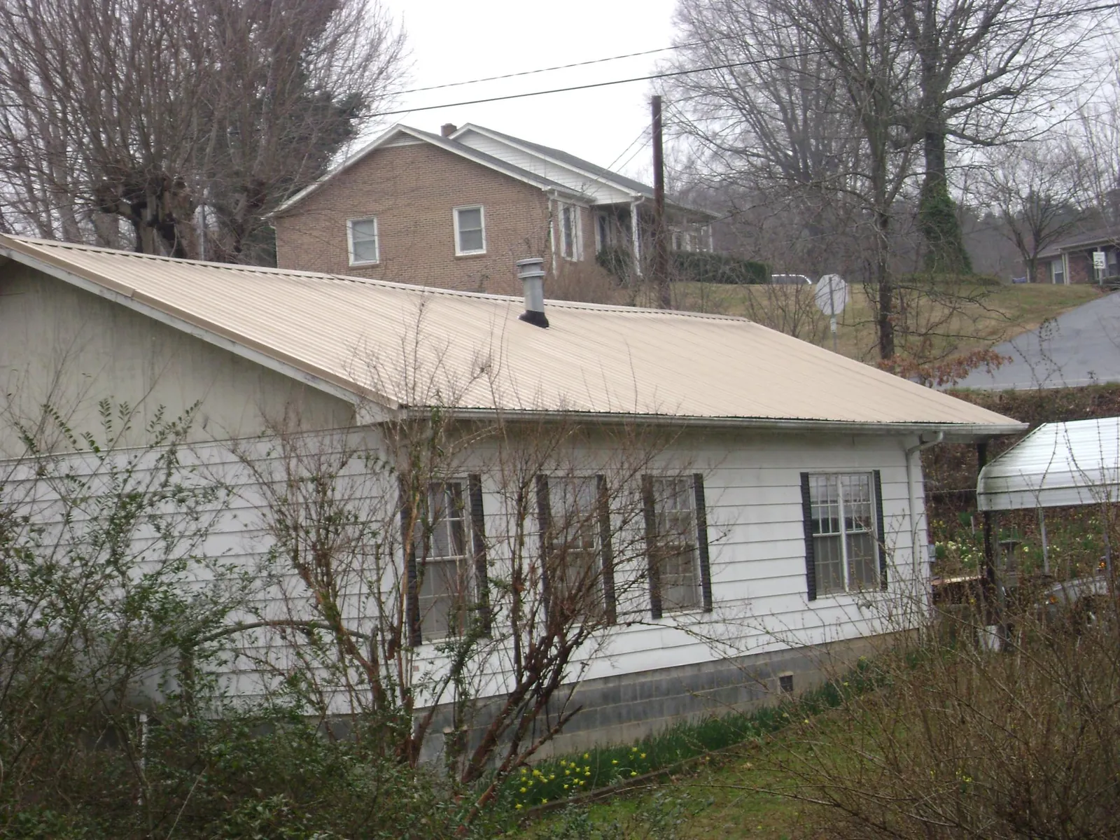 Tan metal roof on a white sided house set into a hillside — Commercial Roofing by Roofing Brothers in Pinson