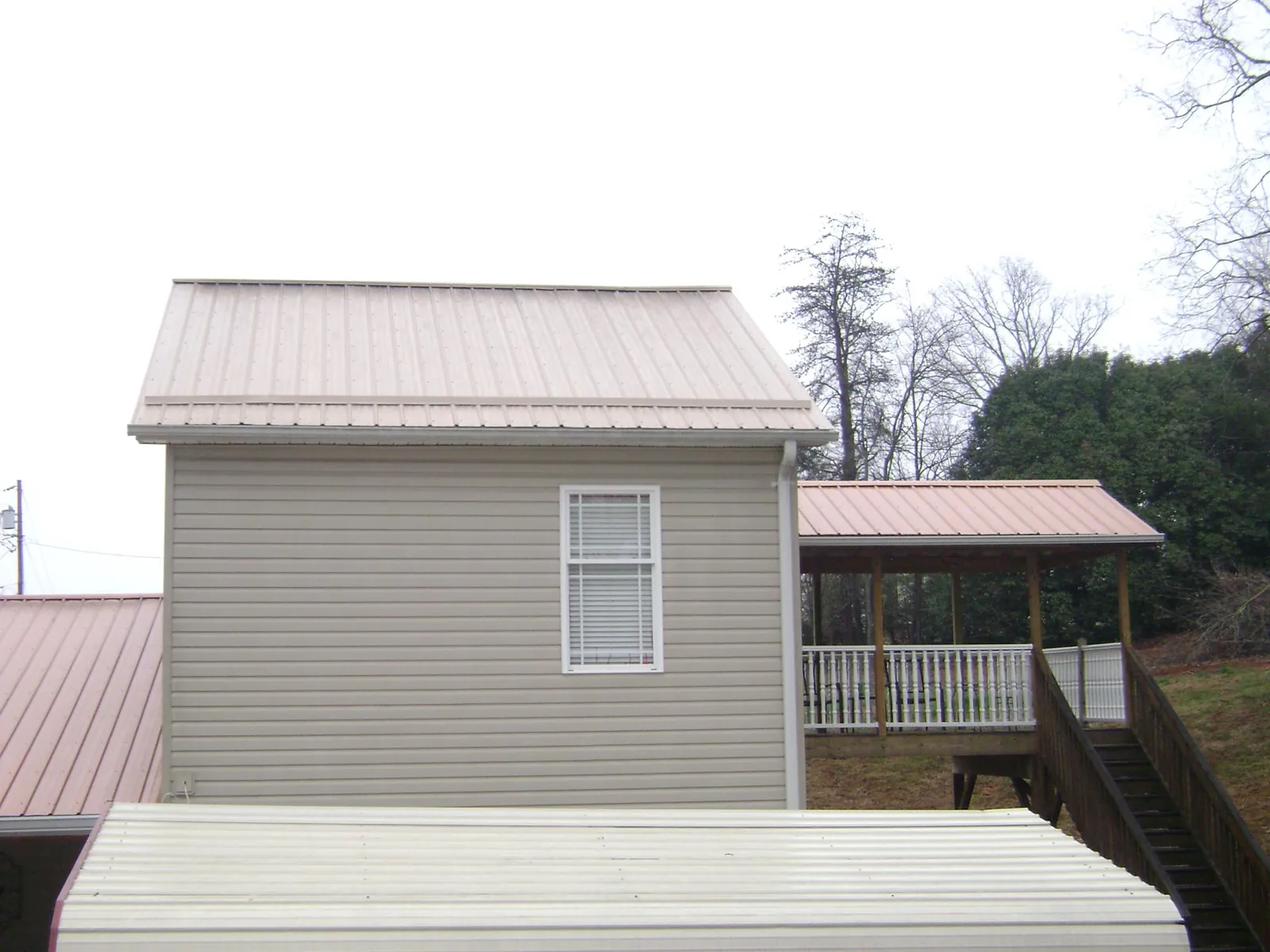 Tan metal roofs on a two story addition and attached porch, from a Roof Replacement job in Pinson